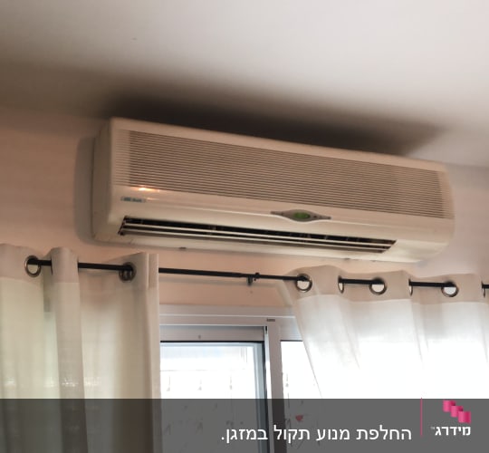 מזגן מותקן על קיר מעל חלון עם וילונות
